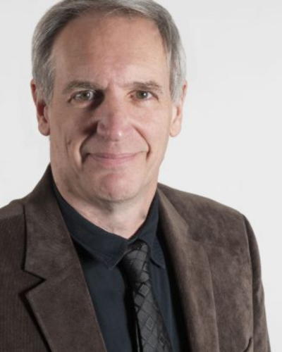 Portrait of an older white man wearing a brown suit; smiling at the camera