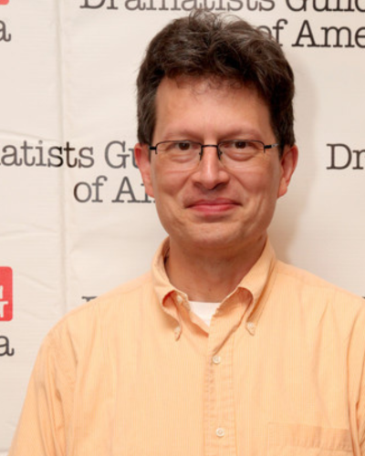 Portrait of a smiling white man with dark hair, wearing a yellow button-down.