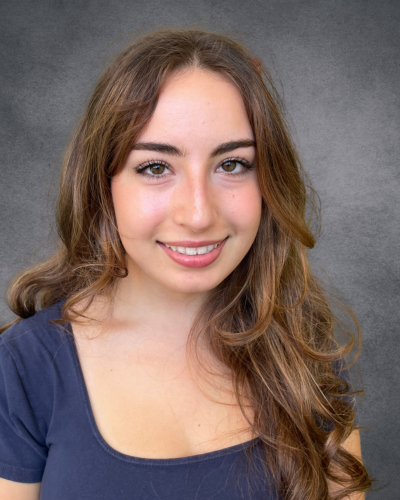 Close-up portrait of a person with long, wavy brown hair and a slight smile, wearing a dark blue top.